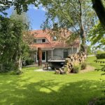 Landhuis met rood dak, gazon, bomen en buitenbad.