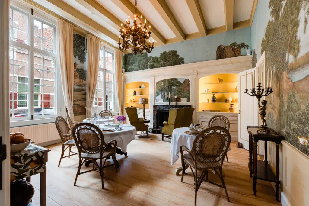 Elegante eetkamer met muurschilderingen, kroonluchters en ronde tafels.
