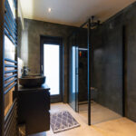 Moderne badkamer met donkere tegels, glazen douche en zwart badkamermeubel.