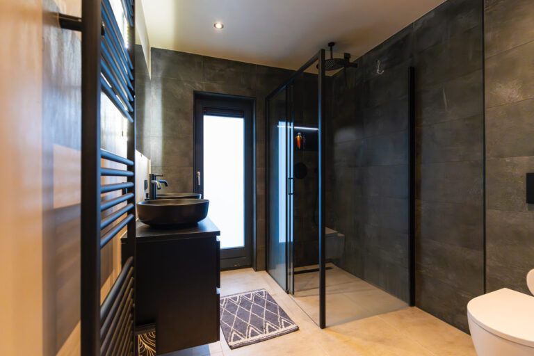 Moderne badkamer met donkere tegels, glazen douche en zwart badkamermeubel.