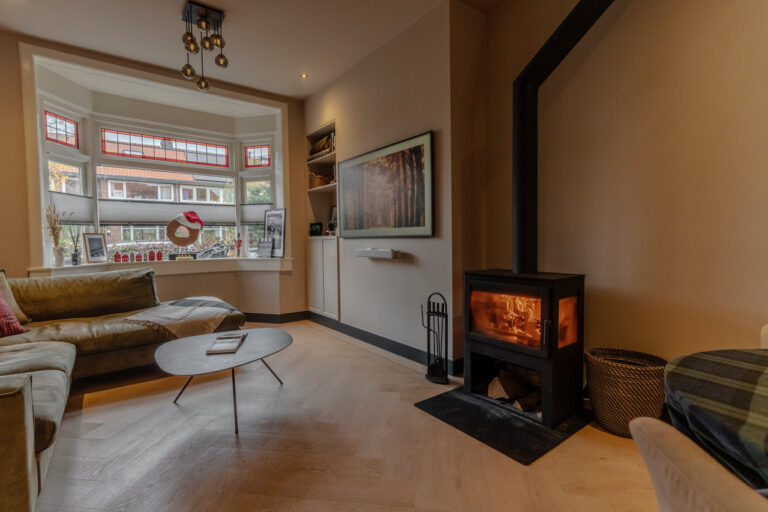 Lichte woonkamer met open haard, fauteuil en voorraam