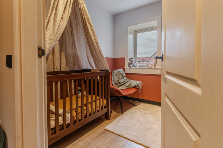 Gezellige babykamer met ledikant, hemel en zitplek bij het raam