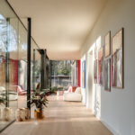 Zonnige gang met glazen wanden, ingelijste kunst en lichte houten vloer.