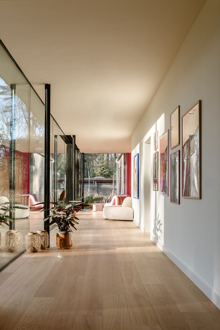 Zonnige gang met glazen wanden, ingelijste kunst en lichte houten vloer.
